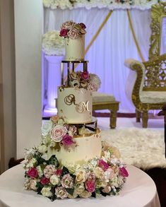 a three tiered wedding cake with pink and white flowers on the table in front of a chair