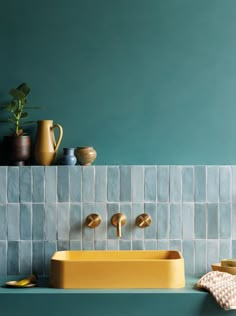 a bathroom with blue tiles and yellow fixtures on the counter top, along with potted plants