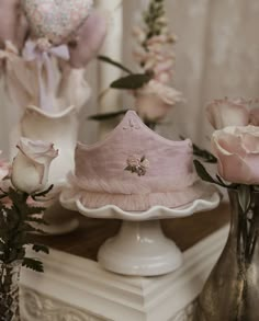 pink flowers are in vases next to a white cake on a pedestal with a crown on top