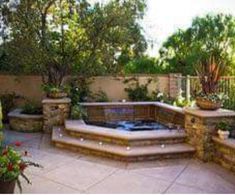 an outdoor hot tub surrounded by stone steps and plants in the back yard with potted trees on either side