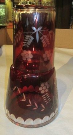 a red glass vase sitting on top of a white tablecloth covered table with other items in the background