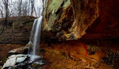 there is a small waterfall in the middle of this cliff with rocks and trees around it