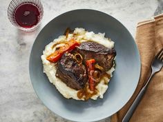 a blue plate topped with meat and mashed potatoes next to a glass of wine