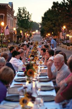 a group of people sitting around a long table with plates and glasses on top of it