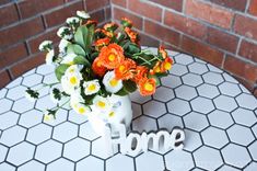 a vase filled with flowers sitting on top of a white tiled table next to a brick wall