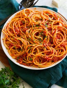 a white bowl filled with spaghetti on top of a wooden cutting board next to a knife and fork