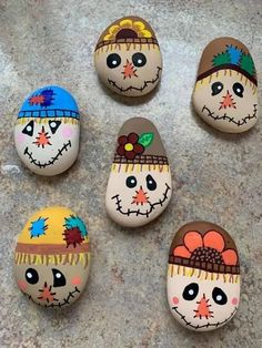 six painted rocks with faces on them sitting on the ground in front of a wall