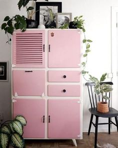 a pink cabinet sitting next to a chair and potted plant on top of it