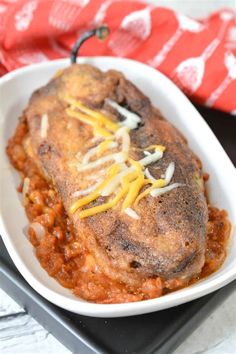 a white bowl filled with meat covered in cheese and sauce on top of a black tray