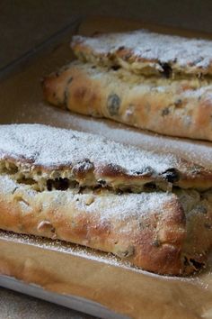 two pastries sitting on top of a wooden cutting board covered in powdered sugar