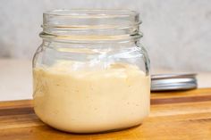 a jar filled with yellow liquid sitting on top of a wooden table next to a spoon