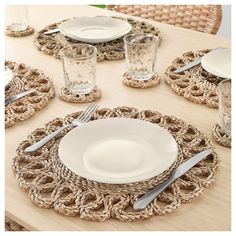 the table is set with plates and silverware on top of woven placemats