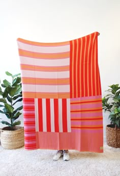 an orange and pink striped blanket sitting on top of a white rug next to potted plants