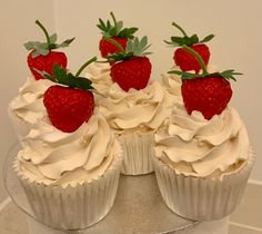 three cupcakes with white frosting and strawberries on top are sitting on a cake plate