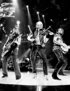 three people on stage with guitars and microphones in their hands, one man is playing the guitar