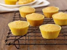 several yellow cupcakes sitting on a cooling rack next to a plate of muffins