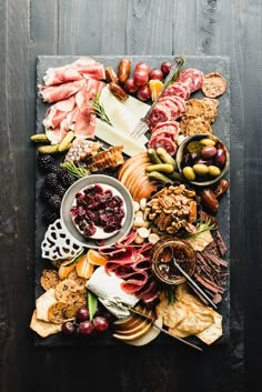 an assortment of meats and cheeses on a slate platter with grapes, nuts, crackers