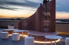 several white tables and stools on a roof at night with the sun setting in the background