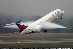 a delta airplane taking off from an airport runway with its landing gear down and spraying water on the ground