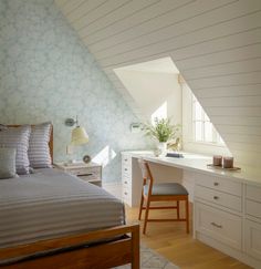 a bed sitting under a window next to a wooden desk and chair on top of a hard wood floor