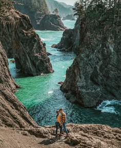 two people standing on the edge of a cliff looking out to sea