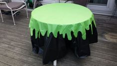 a green and black table cloth on top of a wooden deck with chairs in the background