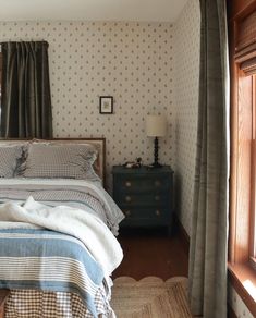 a bed sitting in a bedroom next to a window with curtains on top of it