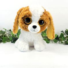 a stuffed dog with big eyes sitting in front of some green leaves on a white surface