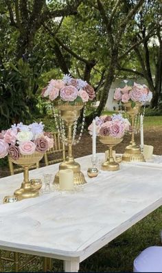 a table topped with gold vases filled with pink and white flowers on top of it