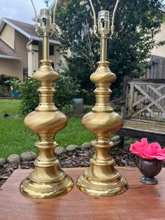 two brass candlesticks sitting on top of a wooden table next to a pink flower