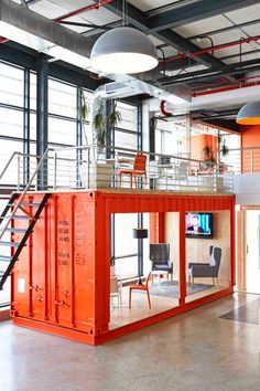 an orange container is in the middle of a large room with stairs and glass windows