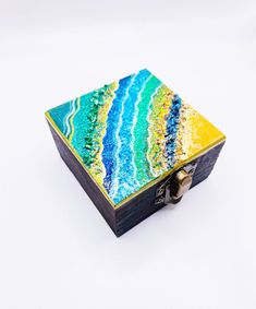 a small wooden box with an abstract painting on the front and sides, sitting on a white surface