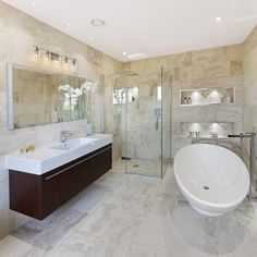 a large bathroom with marble walls and flooring has a bathtub, sink, and shower