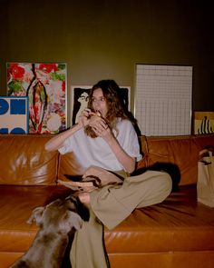 a person sitting on a couch with a dog and eating something out of their hands