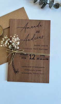 a wooden wedding card with flowers tied to the front and back, on top of two brown envelopes