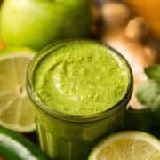 a green smoothie in a glass surrounded by fruit