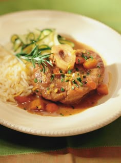 a white plate topped with meat covered in gravy next to rice and vegetables