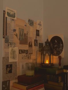 there is a candle on top of some books in front of a wall covered with pictures