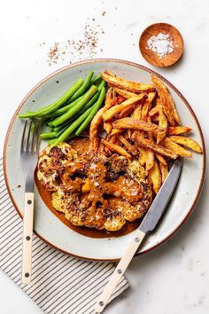 a plate with french fries, green beans and sauce on it next to a fork