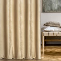 a bed sitting next to a window covered in beige curtain panels and pillows on top of a hard wood floor