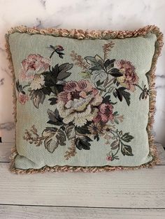 an embroidered pillow with flowers on it sitting on top of a wooden table next to candles