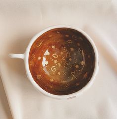 a brown and white cup with gold designs on the inside sitting on a white cloth