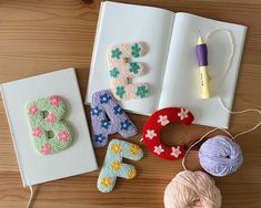 crochet letters and yarn on a table next to an open book with a ball of thread