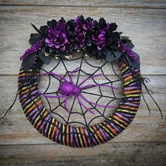 a spider web wreath with purple and black flowers in it on a wooden background,