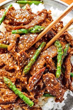 beef and asparagus stir fry on rice in a bowl with chopsticks