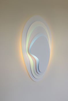 a white wall mounted light with three wavy shapes on it's side and a circular shape in the middle