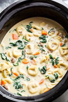 a bowl filled with pasta and spinach soup next to a spoon on top of a table