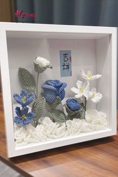 crocheted flowers are displayed in a shadow box on a wooden table with writing