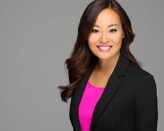 a woman wearing a black blazer and pink shirt is smiling at the camera while standing in front of a gray background