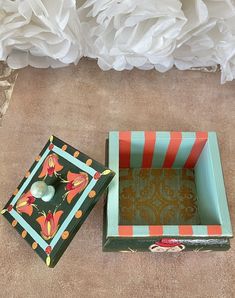 two decorative boxes sitting on the ground next to some white flowers and one is empty